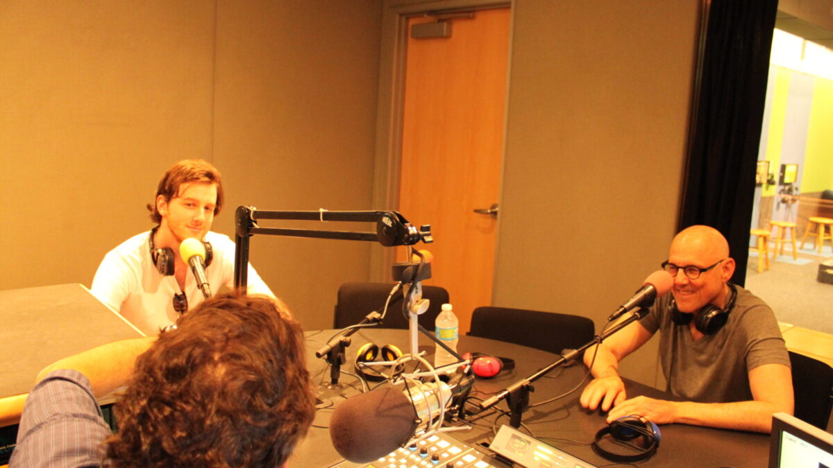 IMG_8750 Two adults speaking into microphones being interviewed by an adult sitting behind a microphone and a mixer in a radio studio