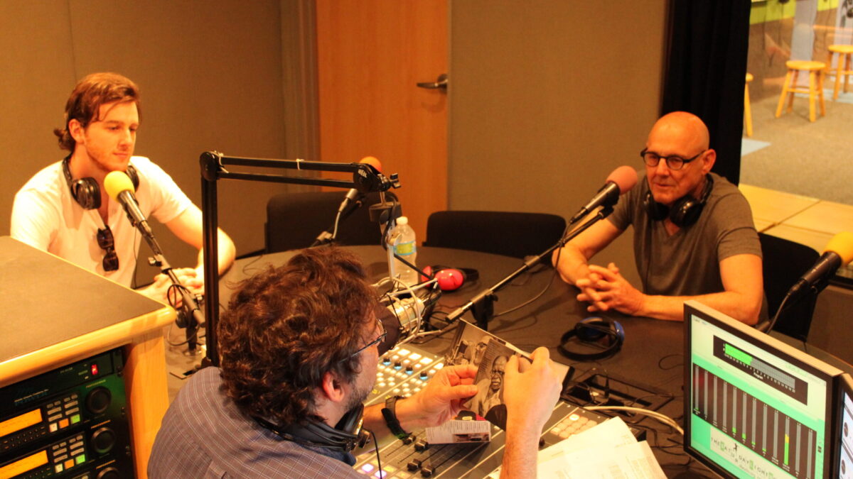 IMG_8752 Two adults speaking into microphones being interviewed by an adult sitting behind a microphone and a mixer in a radio studio