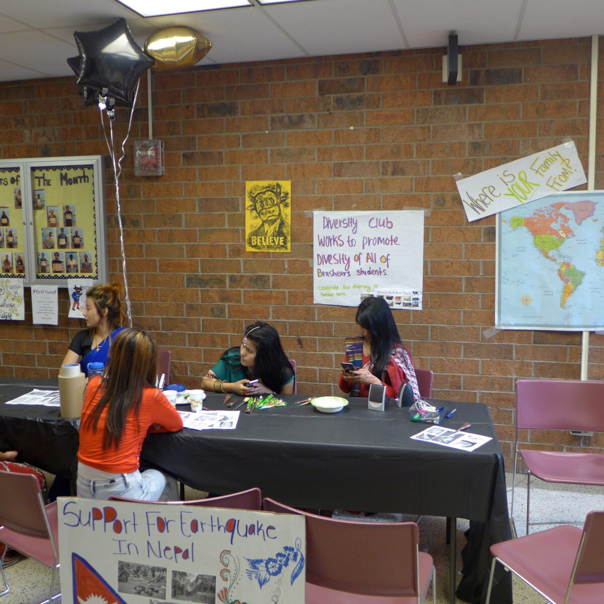 Four teens sitting around a black table in front of a posterboard in a classroom