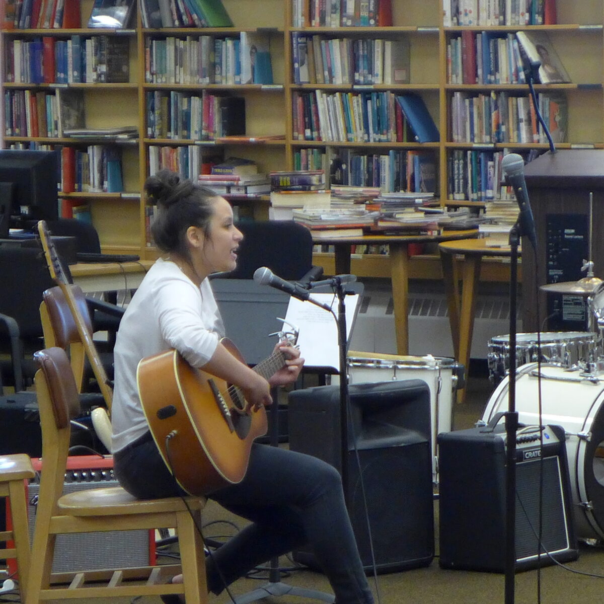 An individual playing an acoustic guitar and singing into a microphone in a library