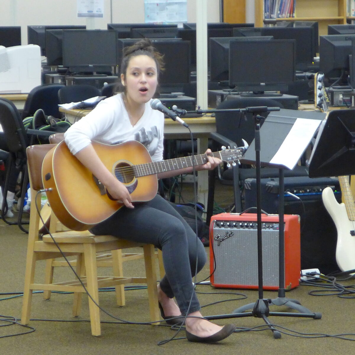 An individual playing an acoustic guitar and singing into a microphone in a library