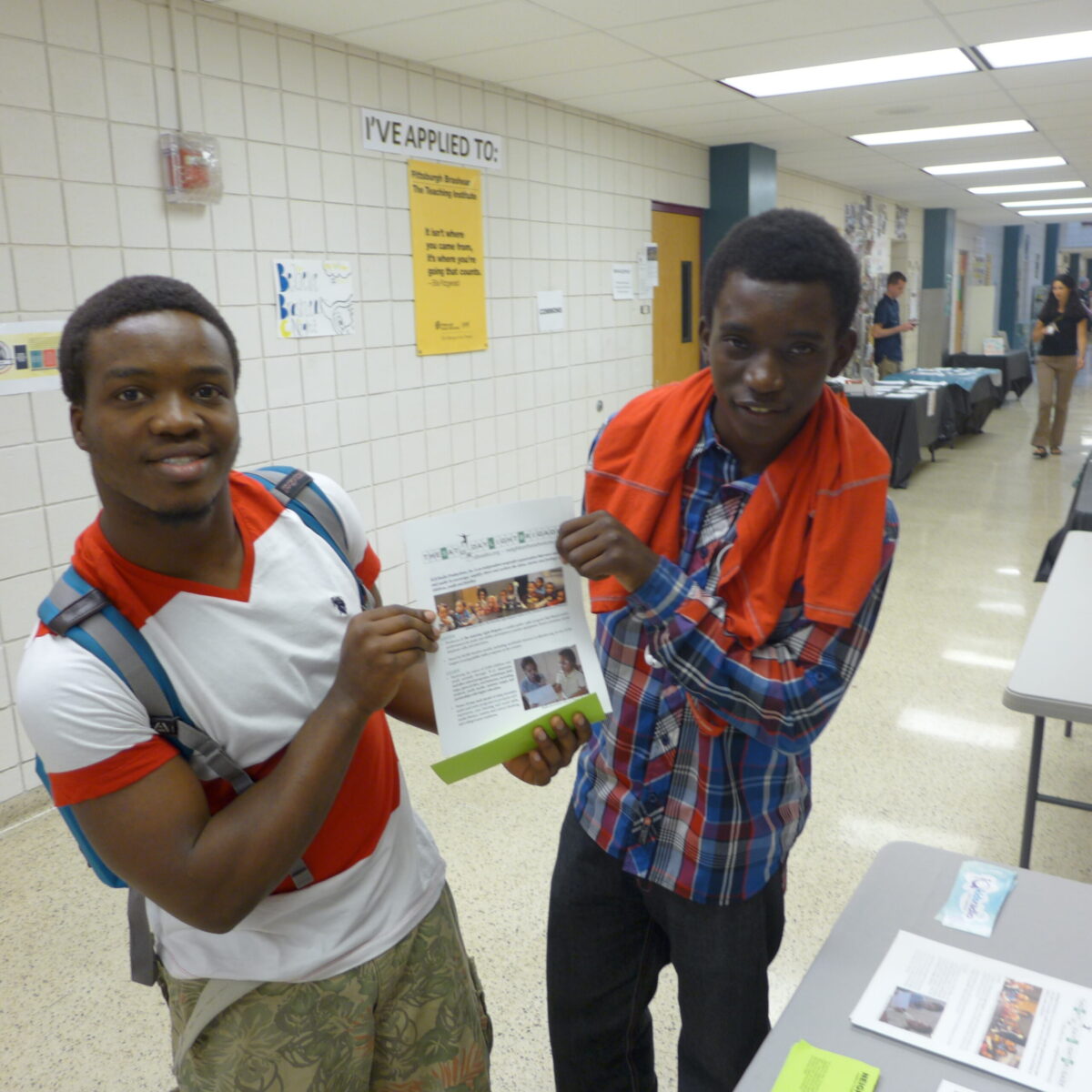 Two teens holding up a piece of paper standing in a school hallway