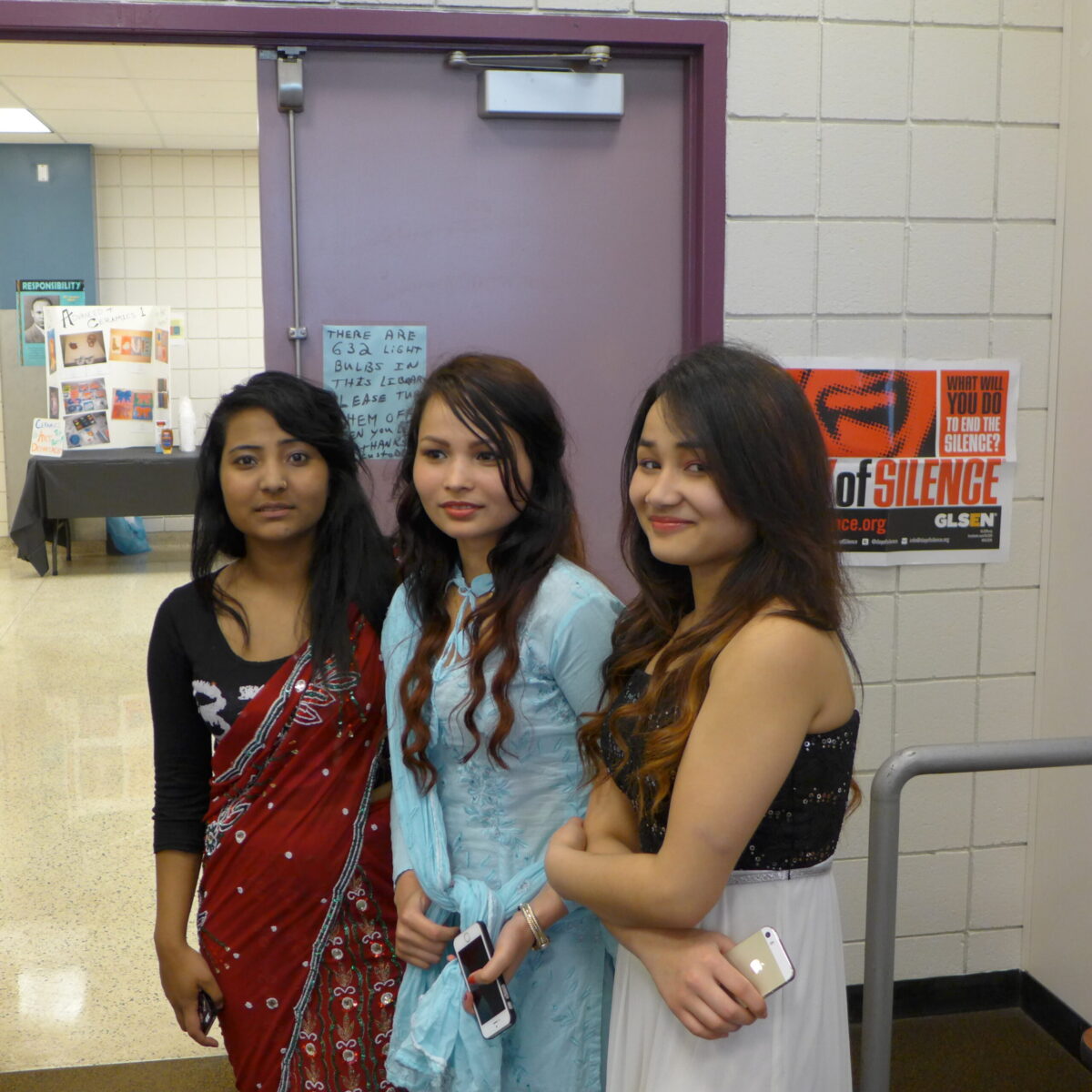 Three teens looking at the camera standing in a school hallway