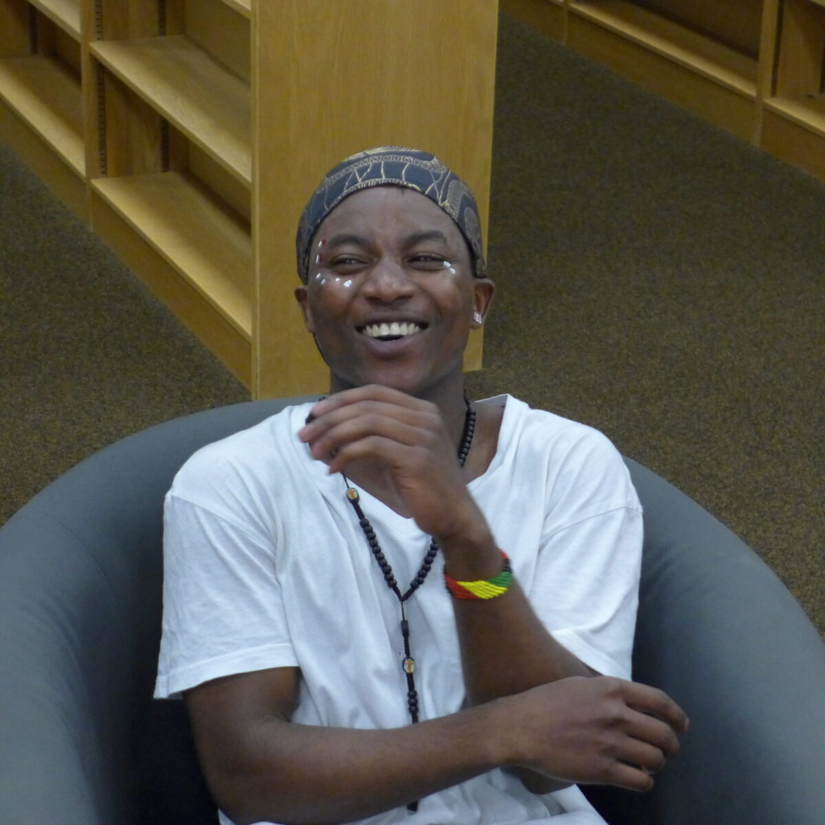 An individual smiling while sitting in a gray chair in a library