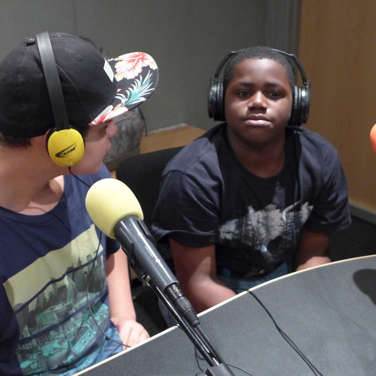 Two youth wearing headphones sitting behind microphones in a radio studio