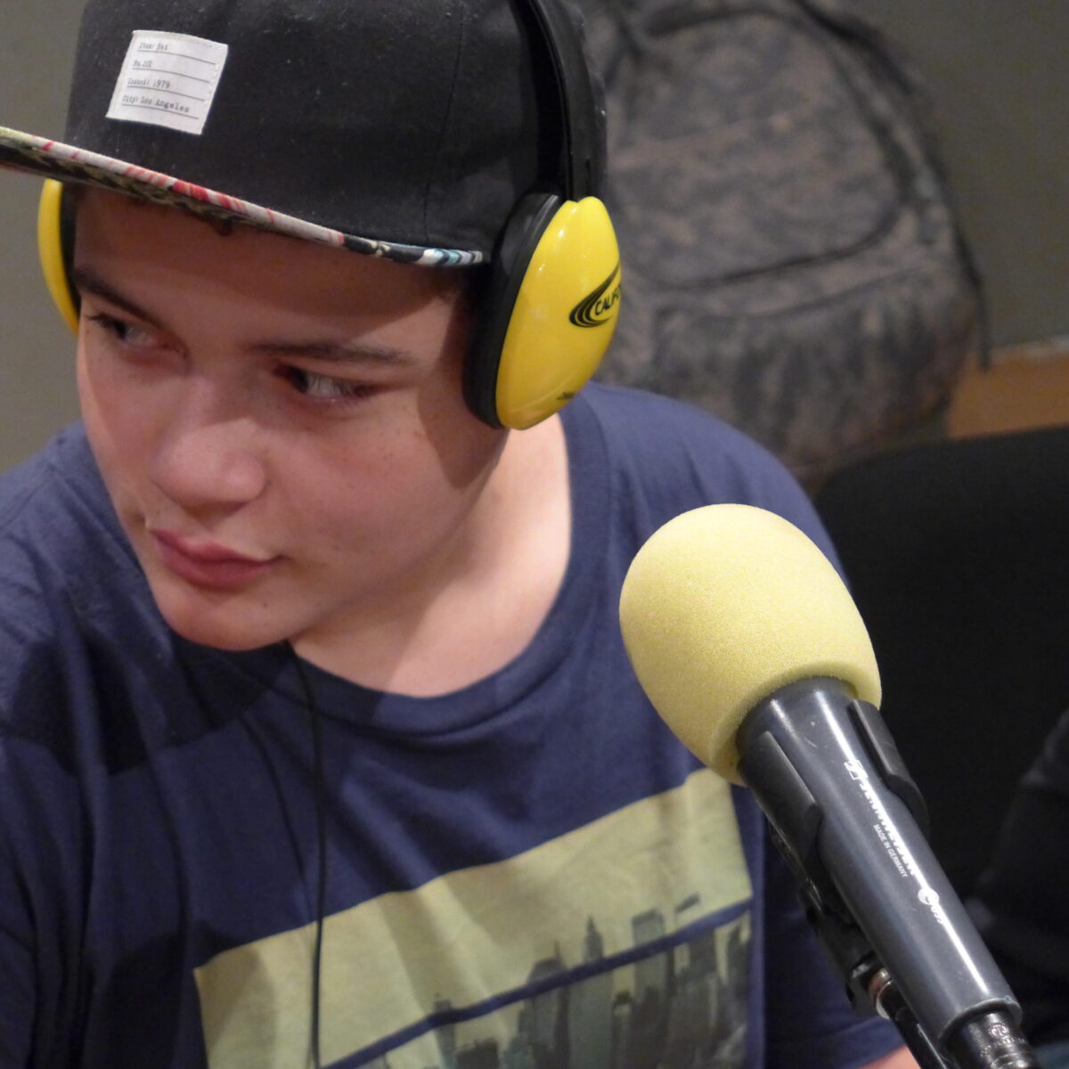 A youth wearing headphones sitting behind a microphone in a radio studio