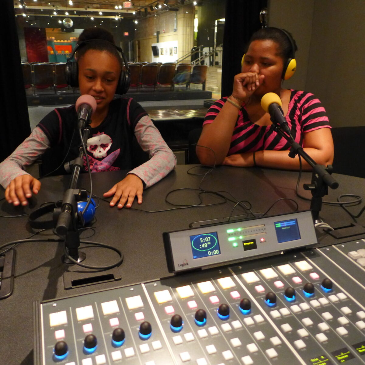 Two youth wearing headphones speaking into microphones in a radio studio