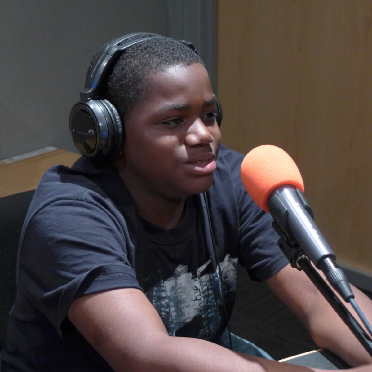 A youth wearing headphones speaking into microphones in a radio studio