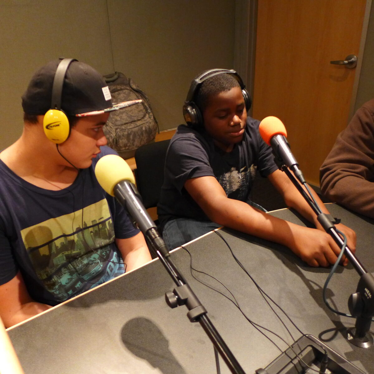 Two youth wearing headphones sitting behind microphones in a radio studio