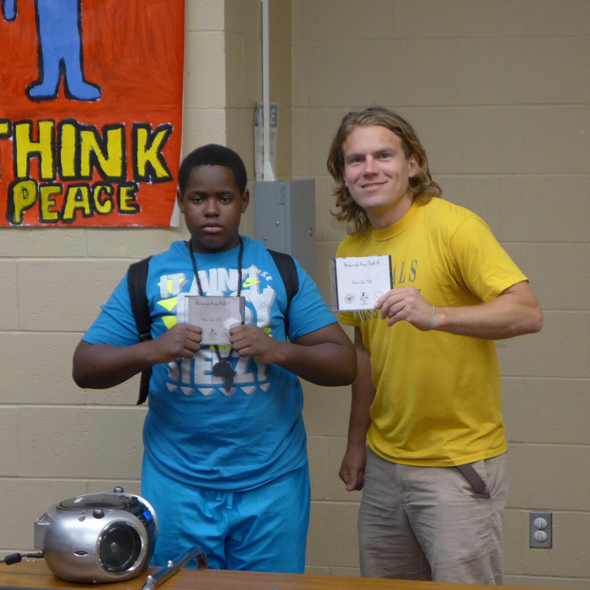 P1020686 A youth and an adult holding up cd cases next to a cd player in a school cafeteria
