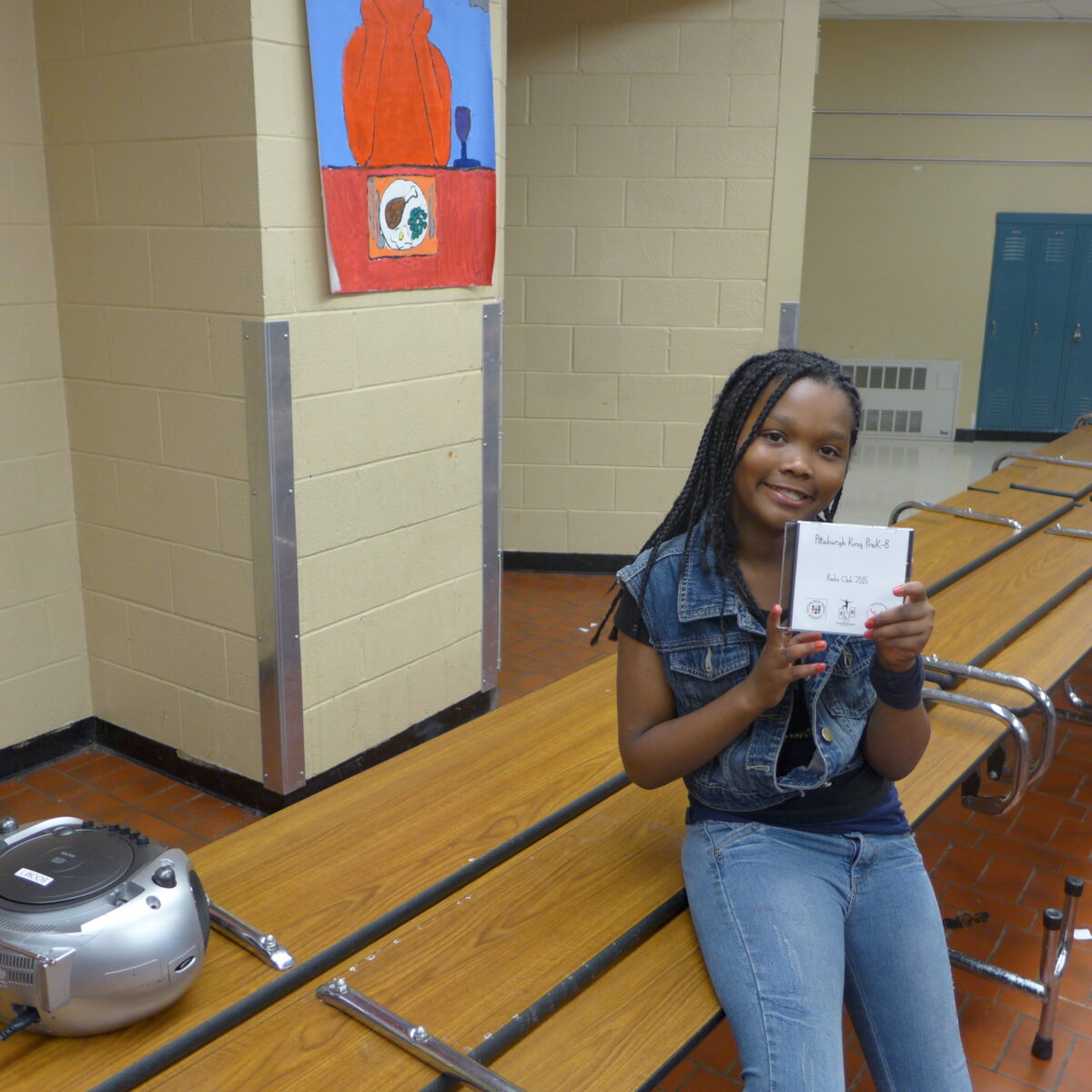 P1020692 A youth holding up a cd case sitting next to a cd player in a school cafeteria