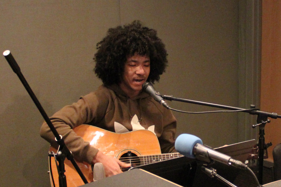 A teen playing acoustic guitar and singing into a microphone in a radio studio