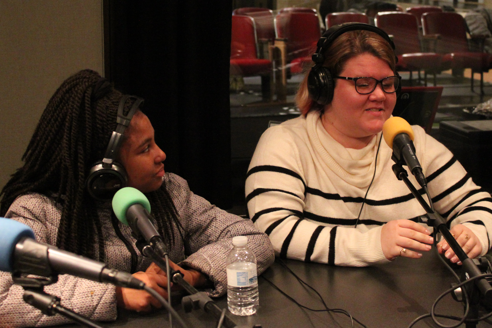Two teens wearing headphones speaking into microphones in a radio studio