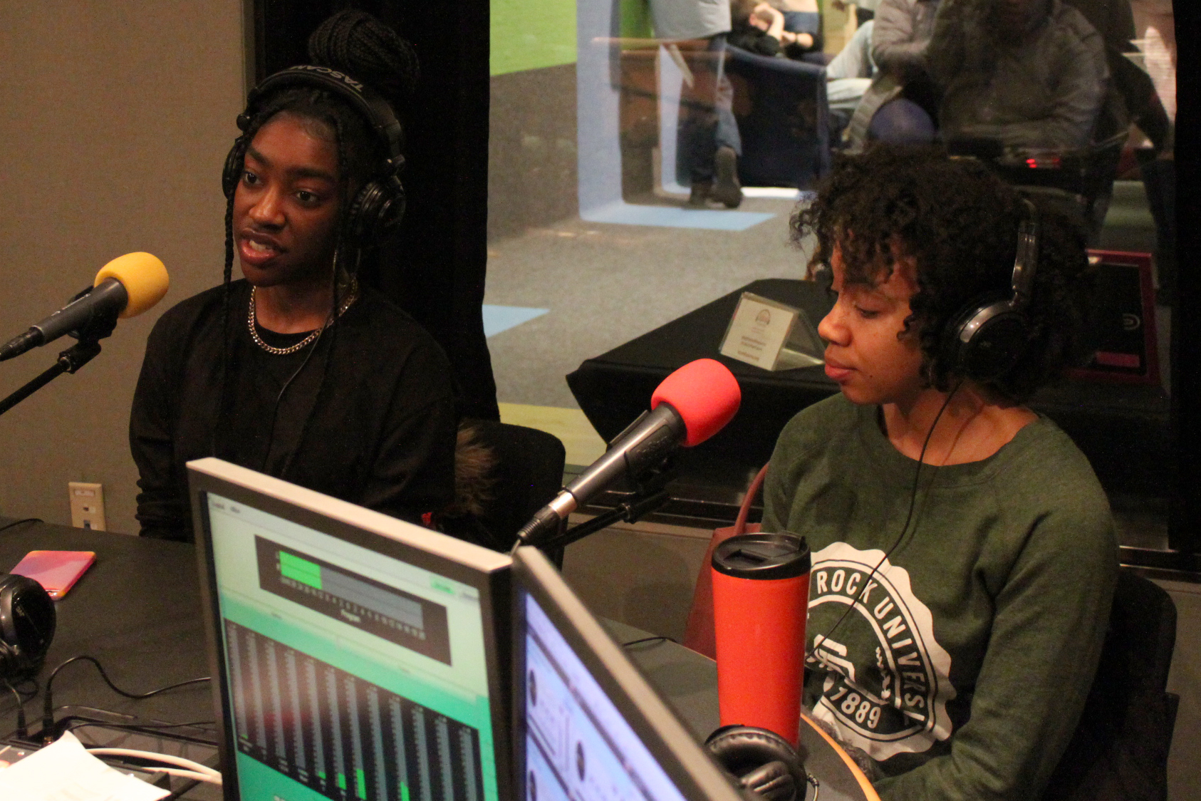 Two teens wearing headphones speaking into microphones in a radio studio