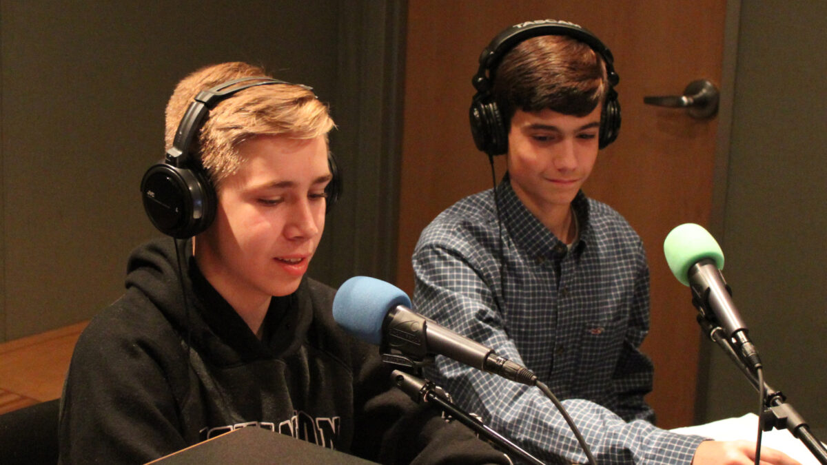 Two teens wearing headphones speaking into microphones in a radio studio