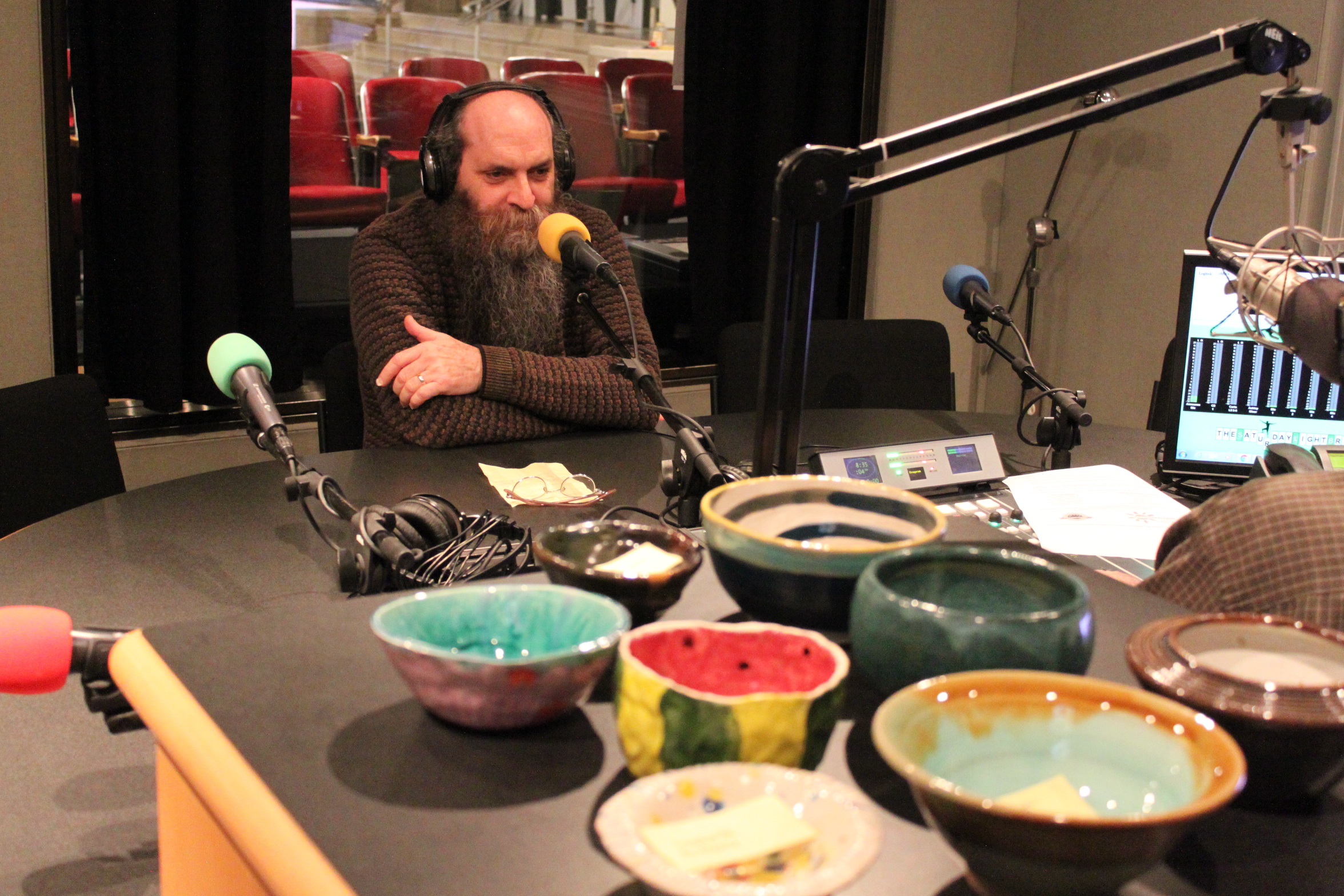An adult wearing headphones speaking into a microphone being interviewed in a radio studio with eight colorful ceramic bowls in the foreground
