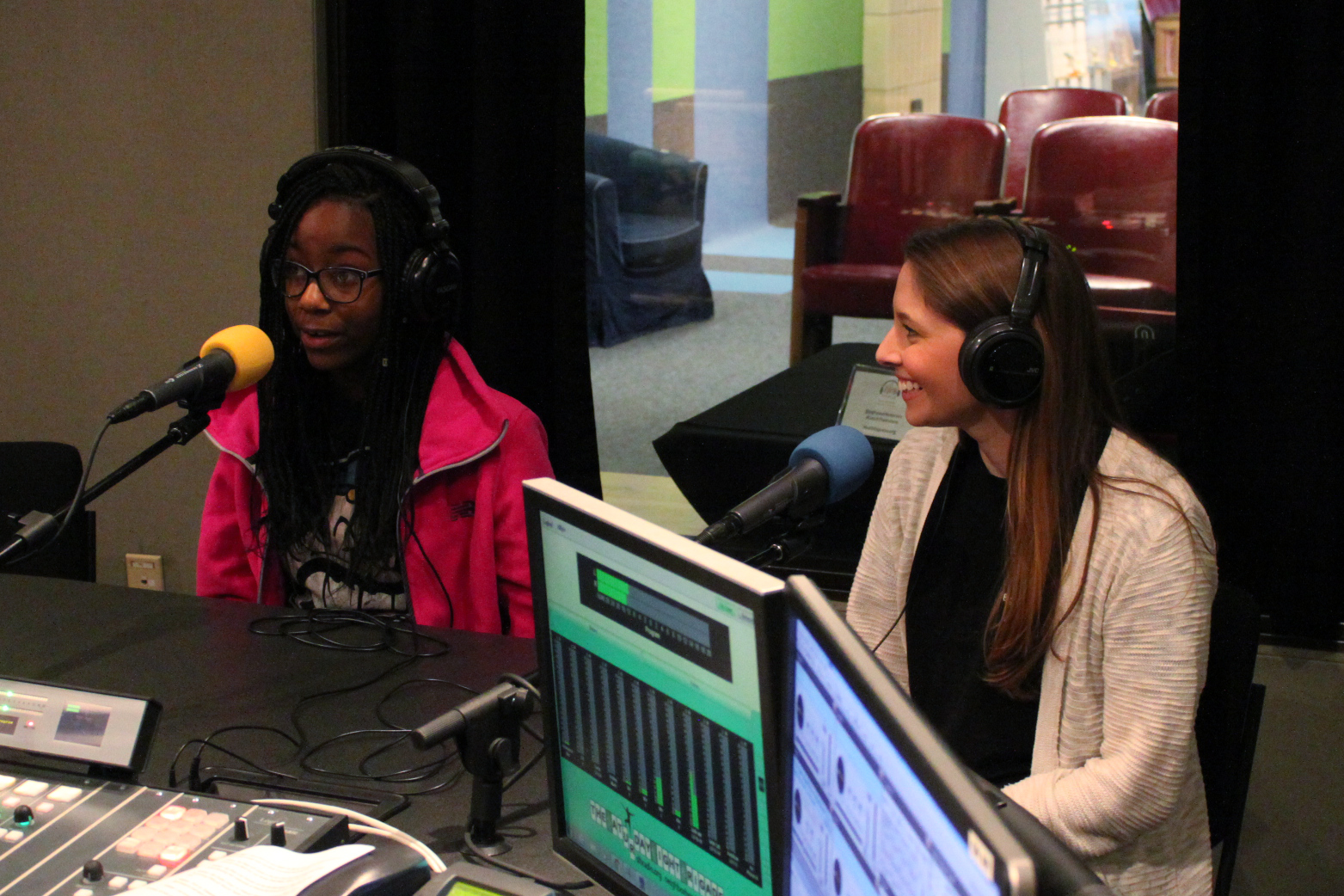 Two teens wearing headphones speaking into microphones in a radio studio