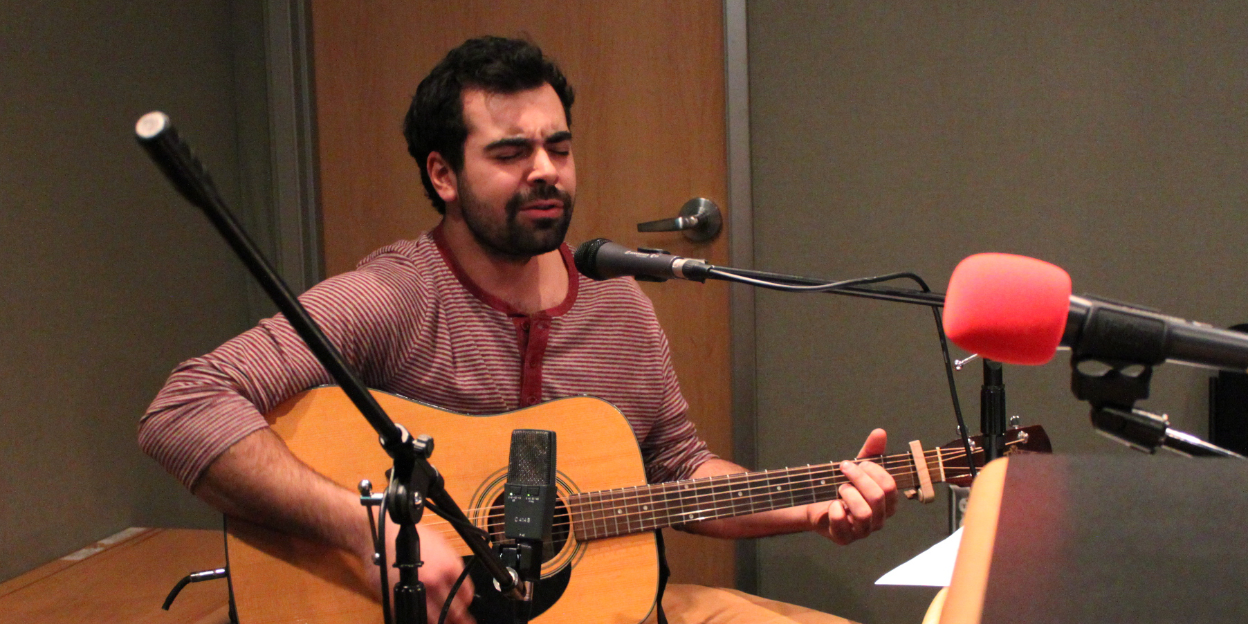 Adult playing acoustic guitar and singing into a microphone in a radio studio