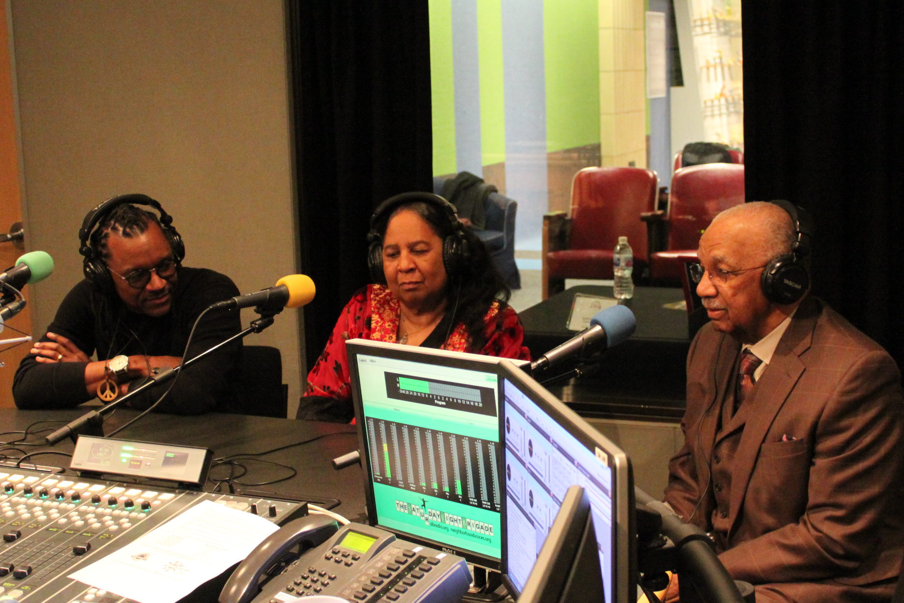 Three adults wearing headphones speaking into microphones being interviewed in a radio studio