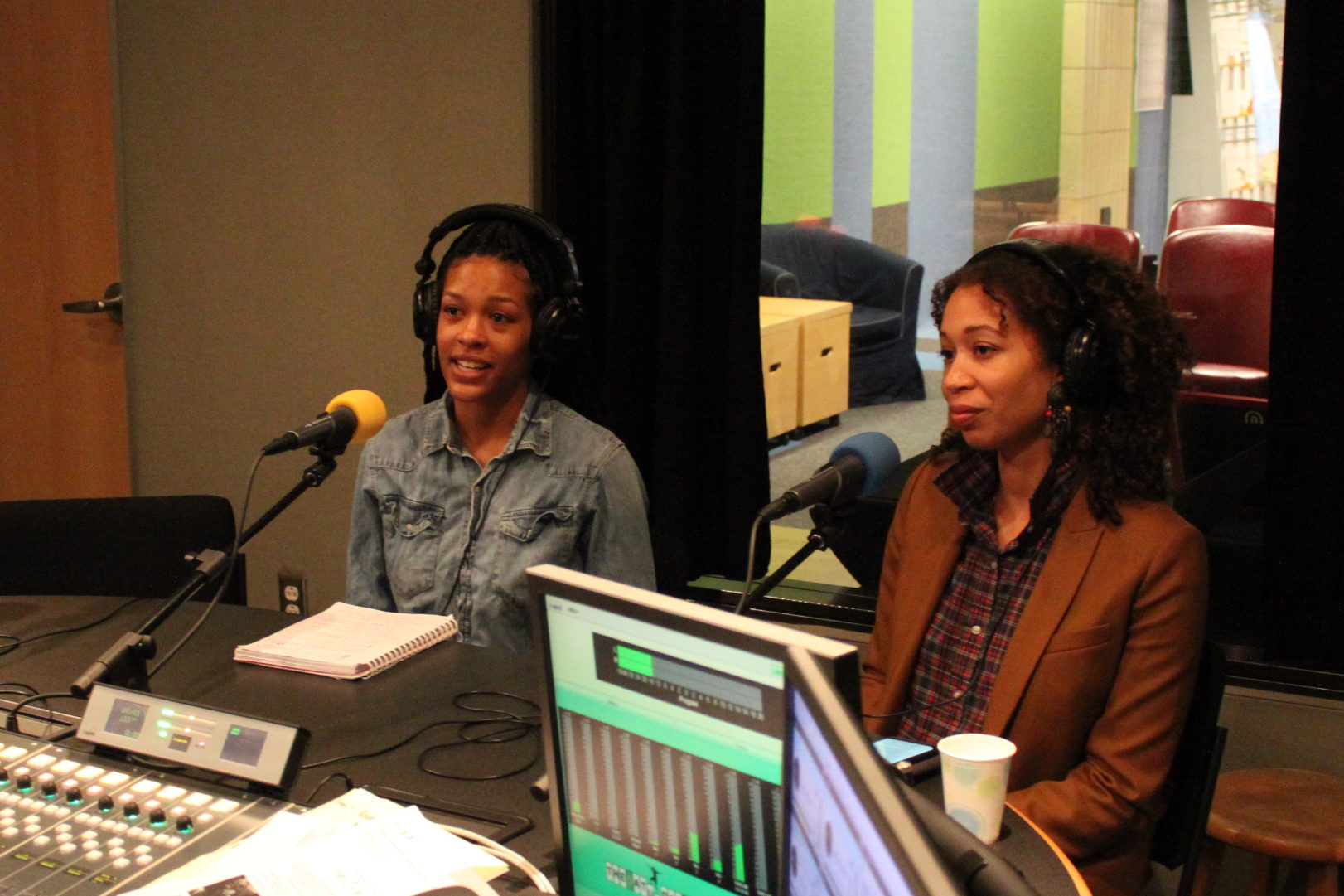 Two individuals wearing headphones speaking into microphones in a radio studio