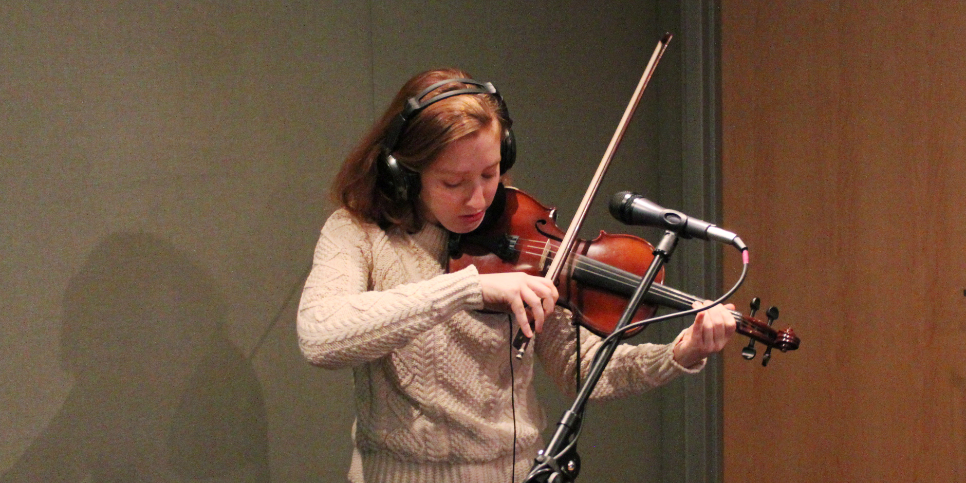 Teen wearing headphones and playing violin into a microphone in a radio studio