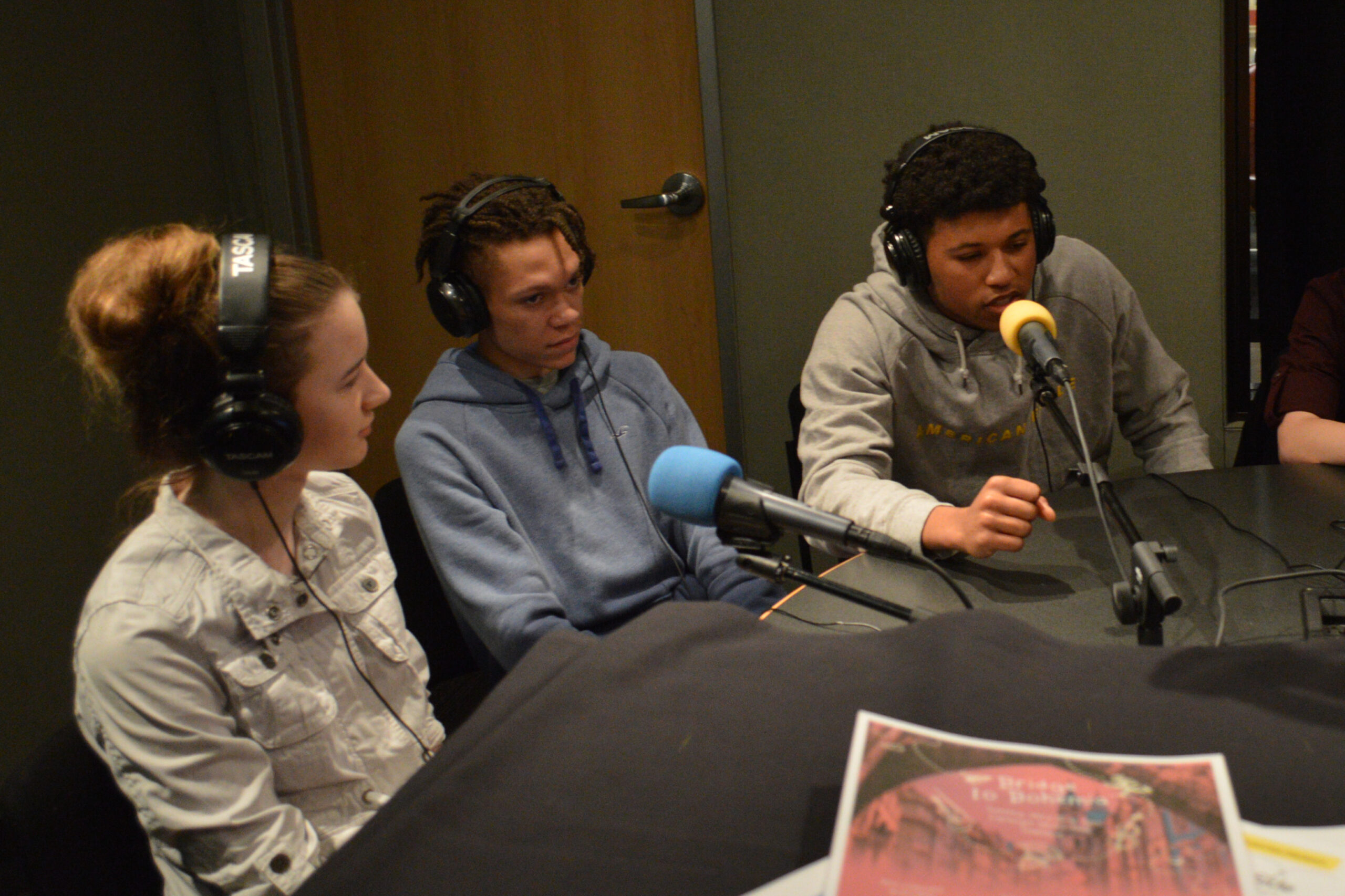 Three teens wearing headphones and speaking into microphones being interviewed in a radio studio