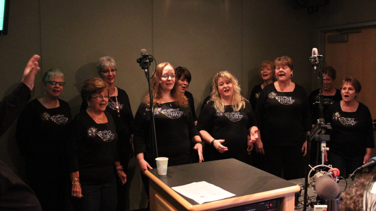 Ten adults singing as a choir into two microphones in a radio studio