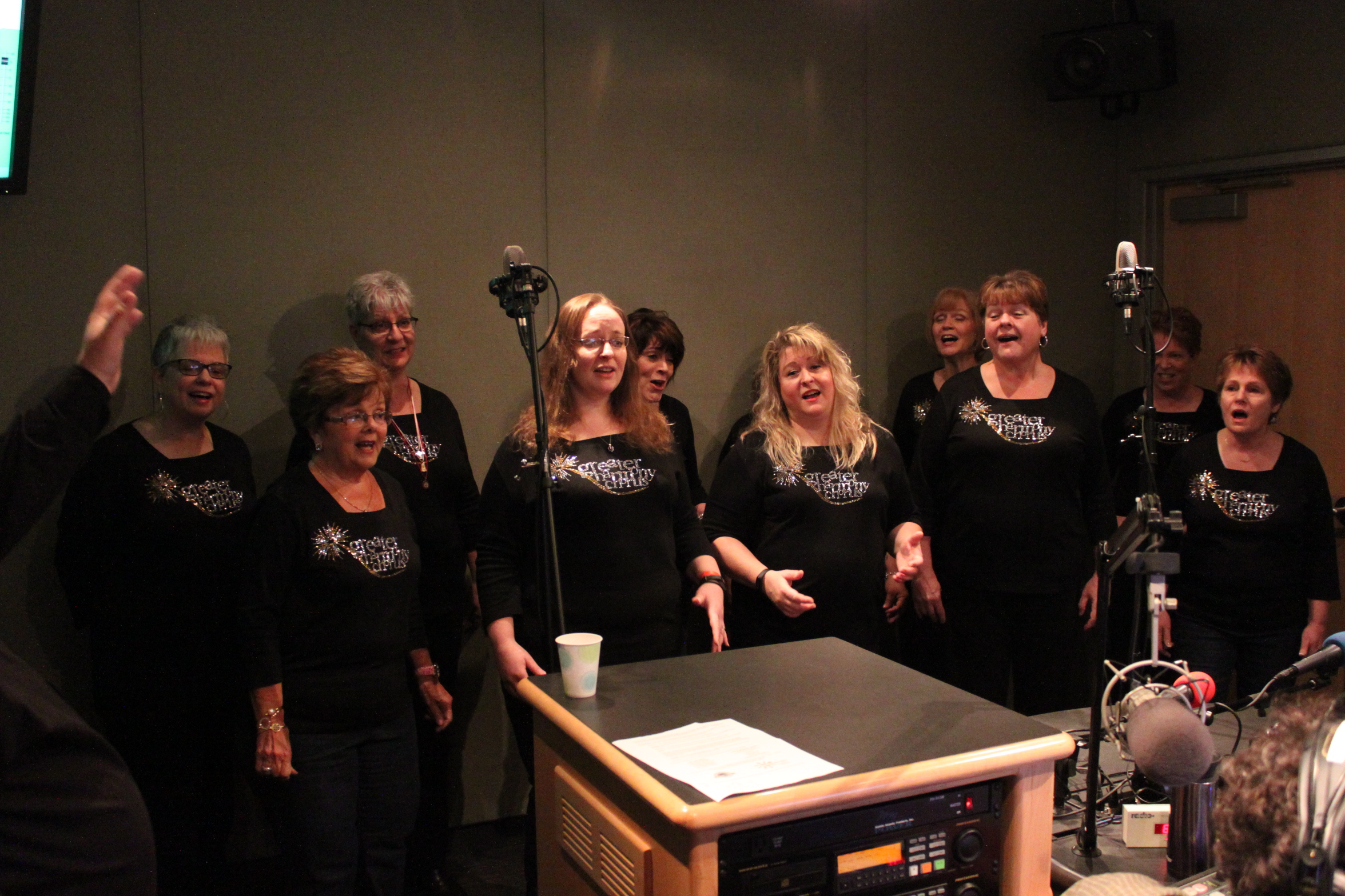 Ten adults singing as a choir into two microphones in a radio studio