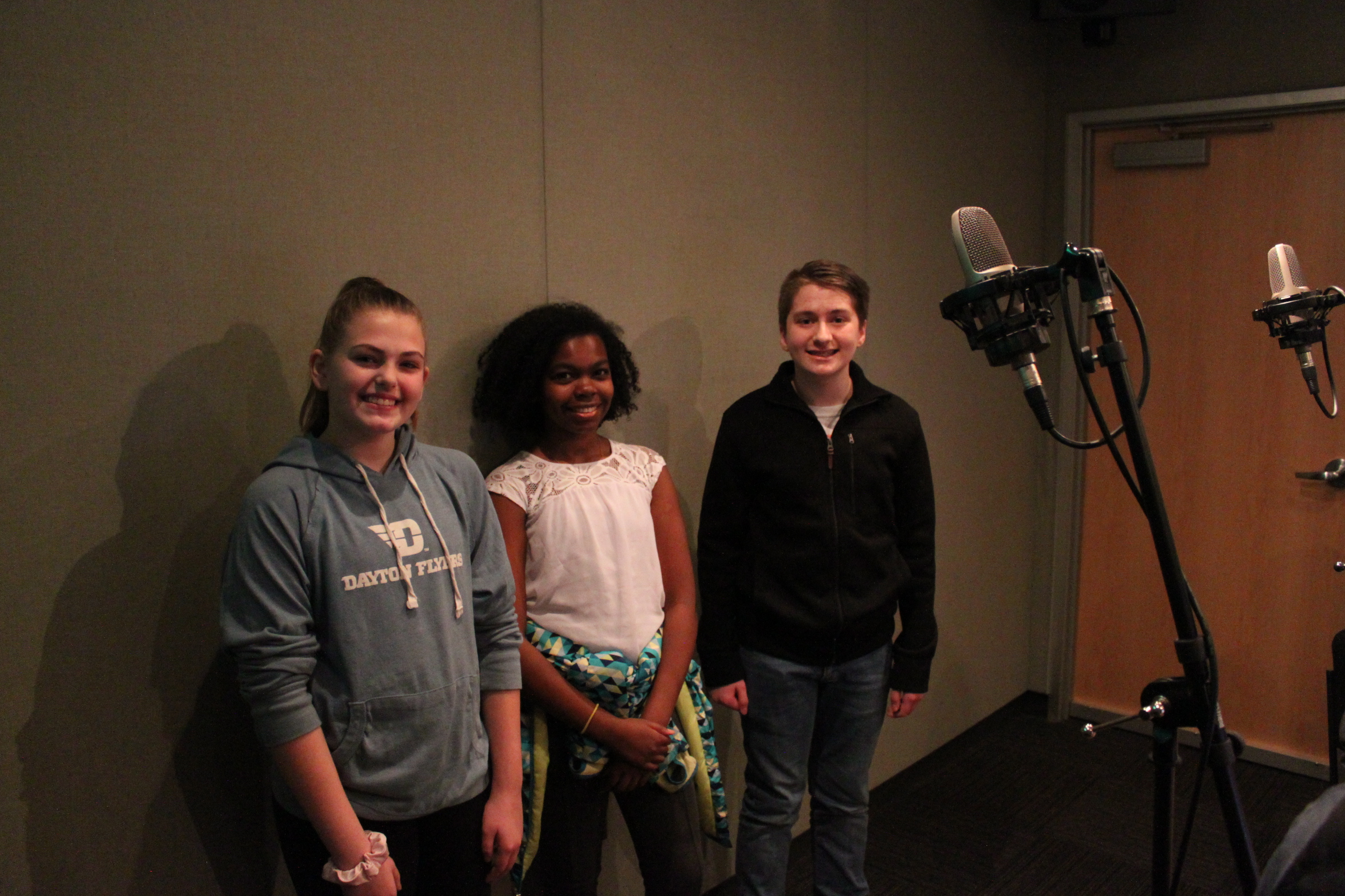 Three youth smiling next to microphones in a radio studio