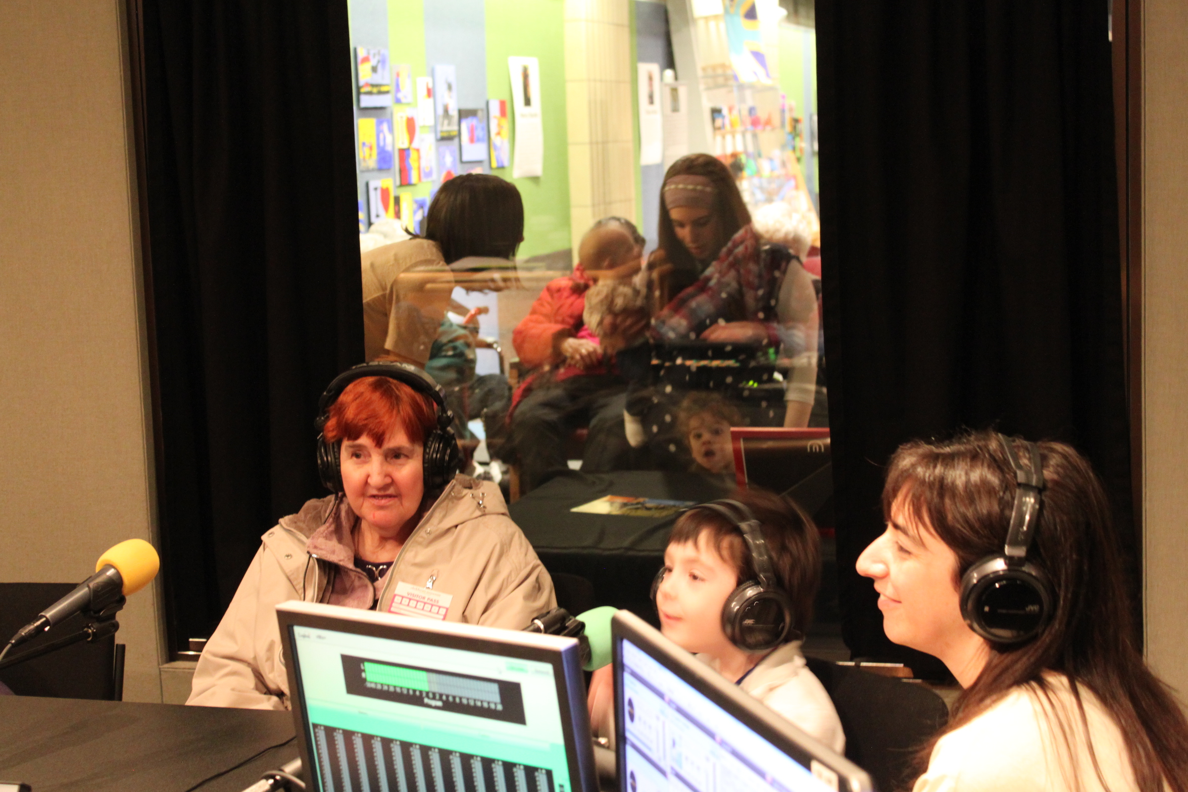 Two adults and a child wearing headphones speaking into microphones in a radio studio