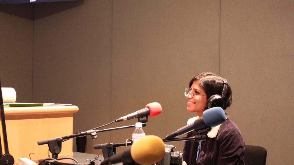 An individual wearing headphones and smiling behind a microphone in a radio studio