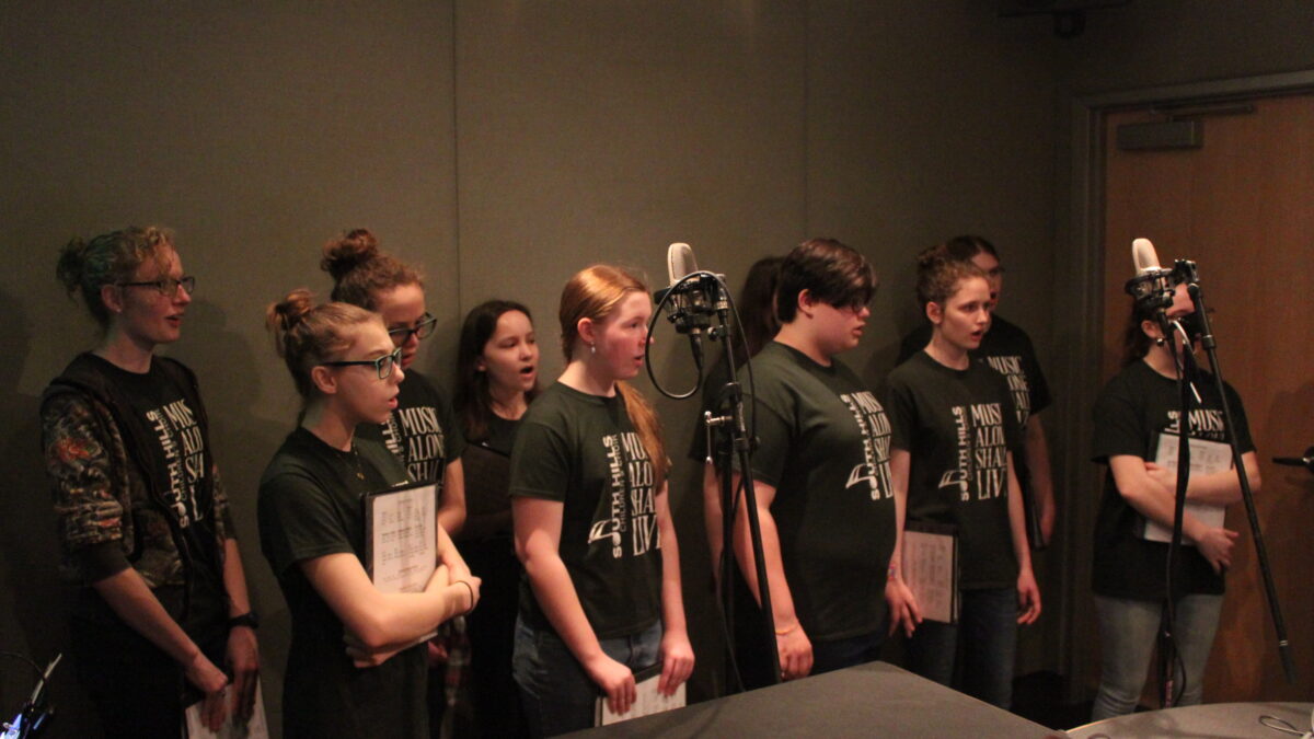 Ten teens singing in a choir in a radio studio