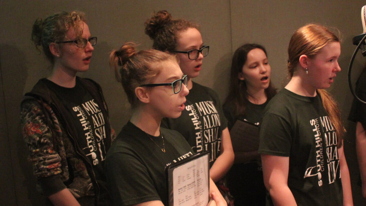 Five teens singing in a choir in a radio studio