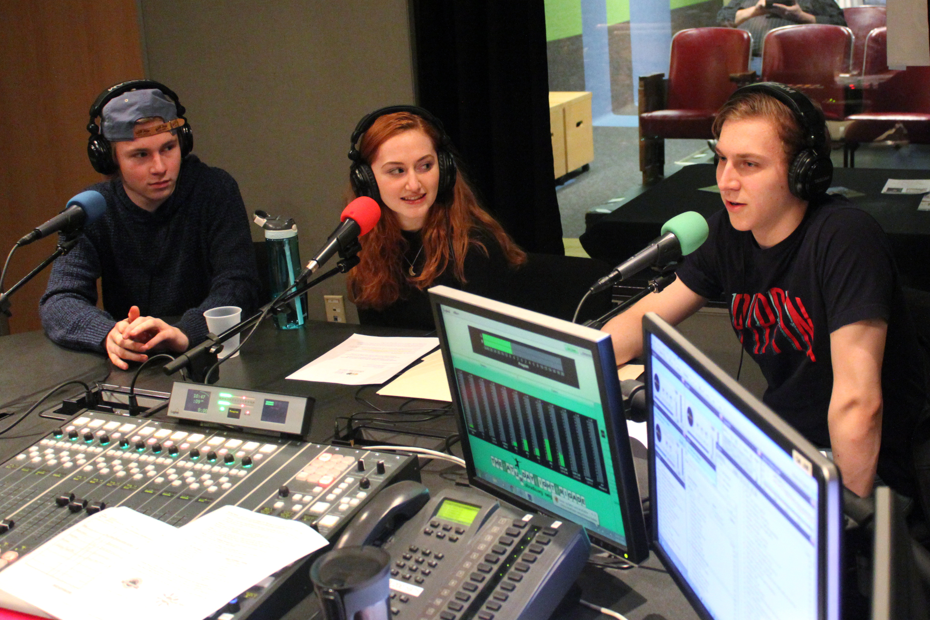 Three teens wearing headphones and speaking into microphones being interviewed in a radio studio