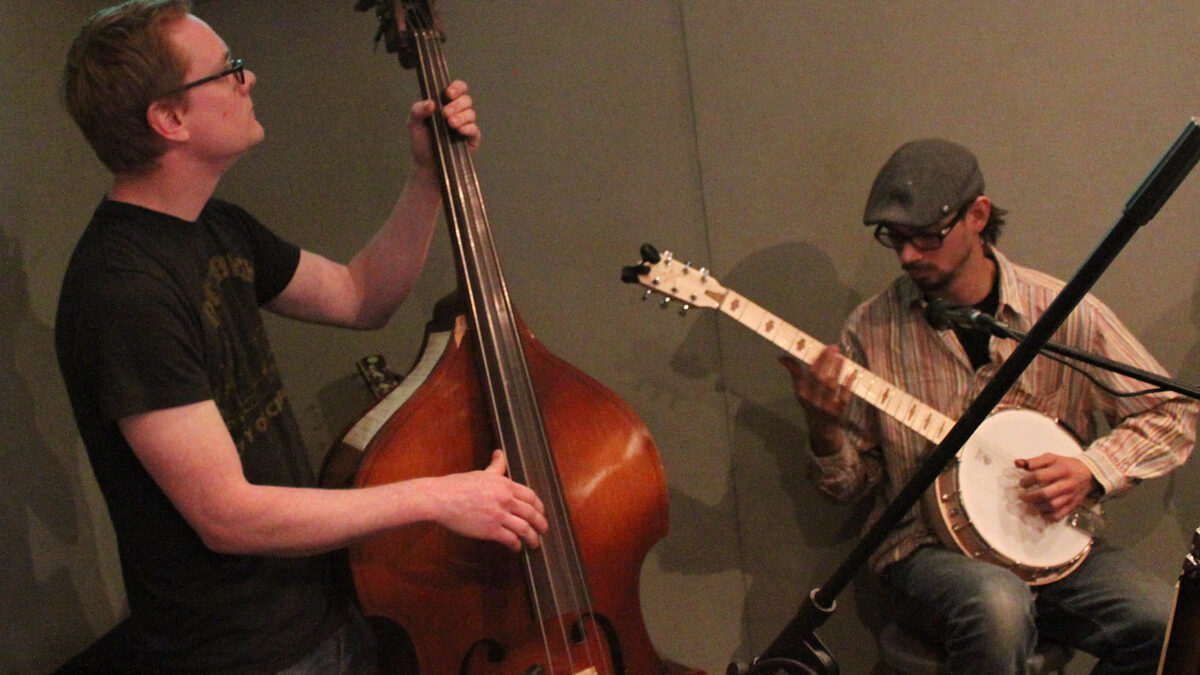 An adult playing upright bass and an adult playing banjo in a radio studio