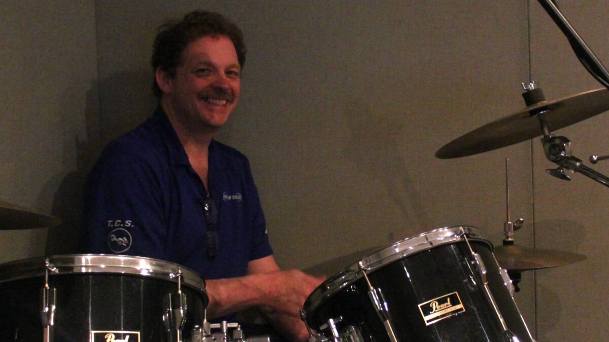 An adult playing a drum set and smiling in a radio studio