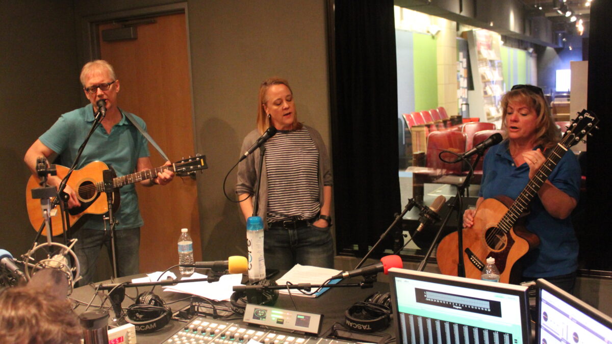 An adult playing acoustic guitar and singing into a microphone, an adult singing into a microphone, and an adult holding an acoustic guitar and singing into a microphone in a radio studio