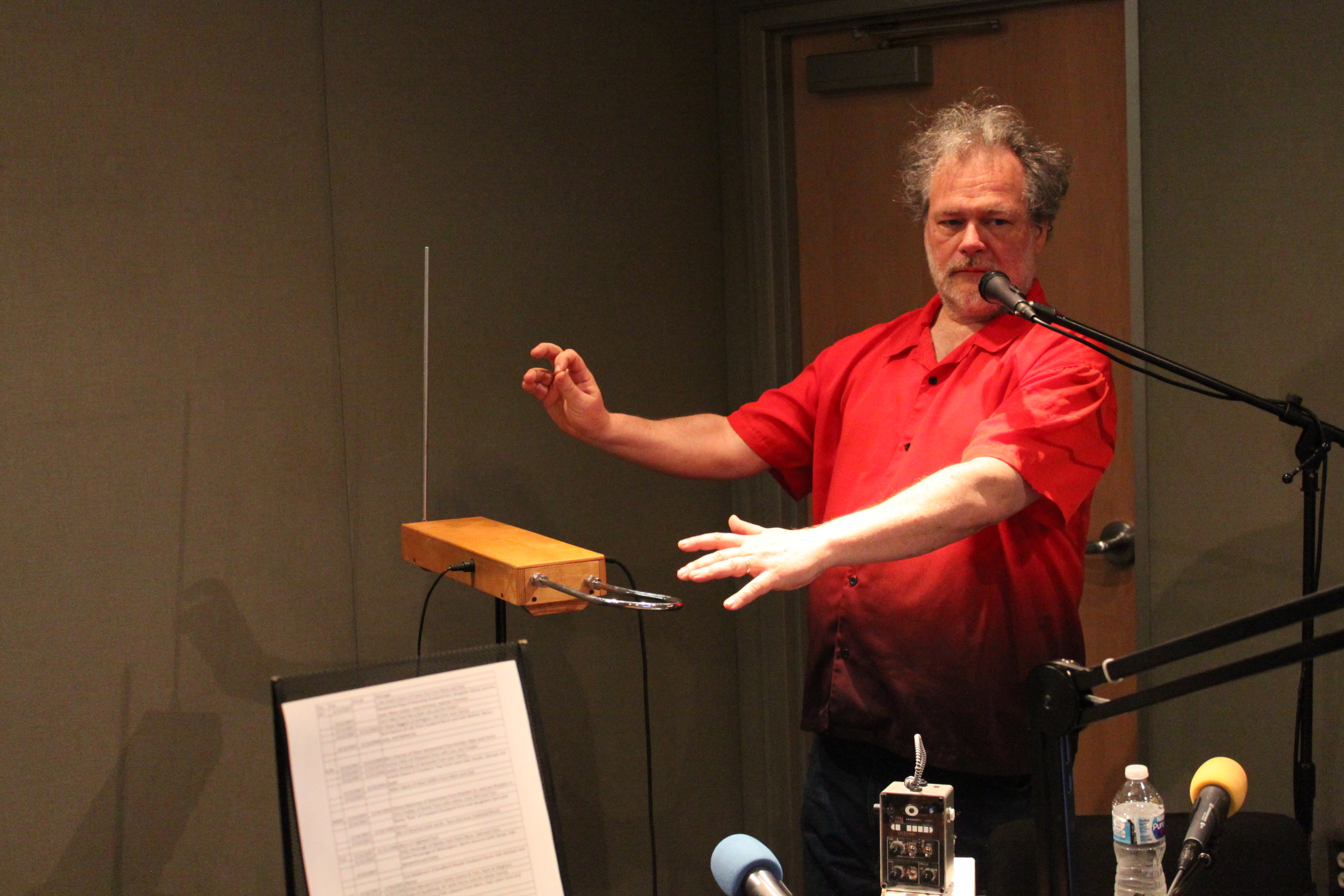 An adult playing a theremin standing behind a microphone in a radio studio