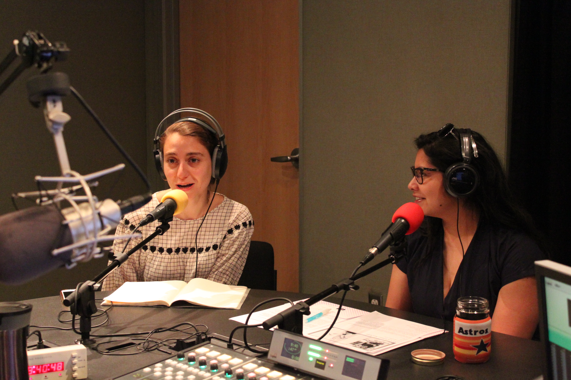 Two adults wearing headphones speaking into microphones being interviewed in a radio studio