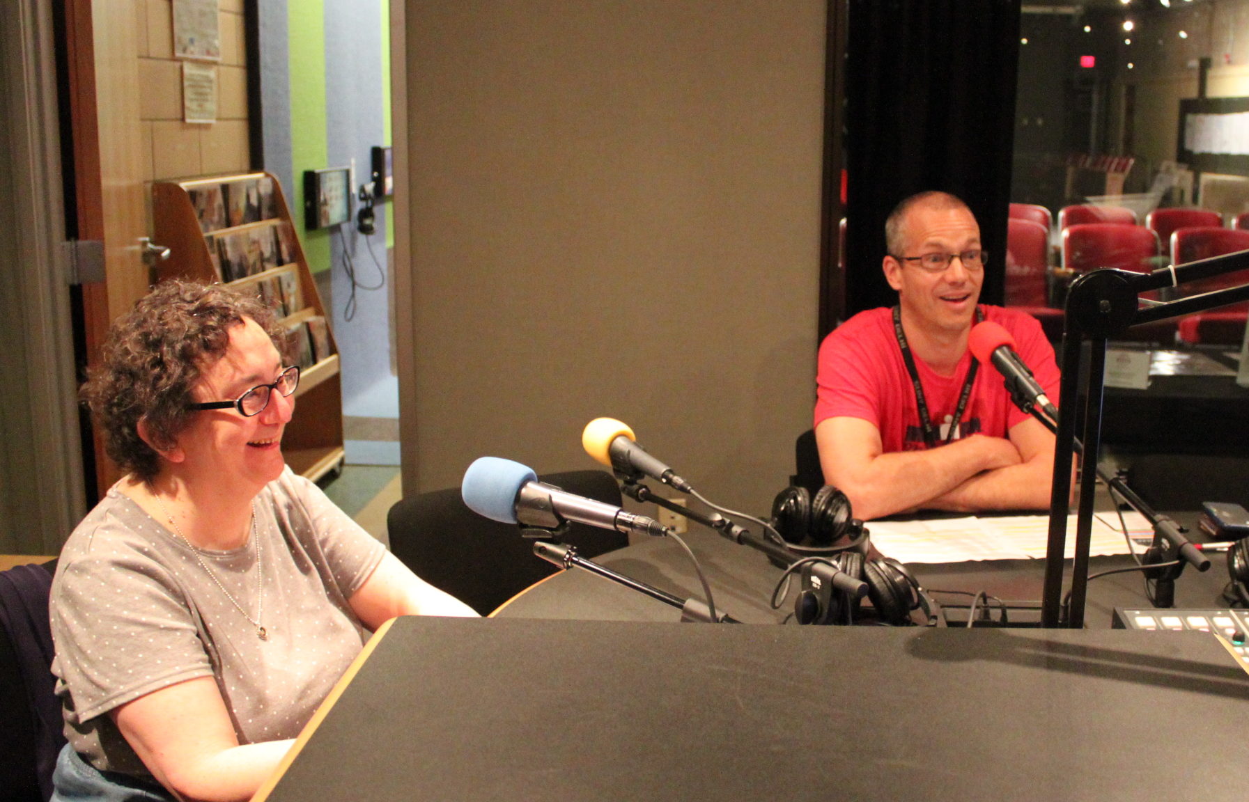 Two adults speaking into microphones in a radio studio