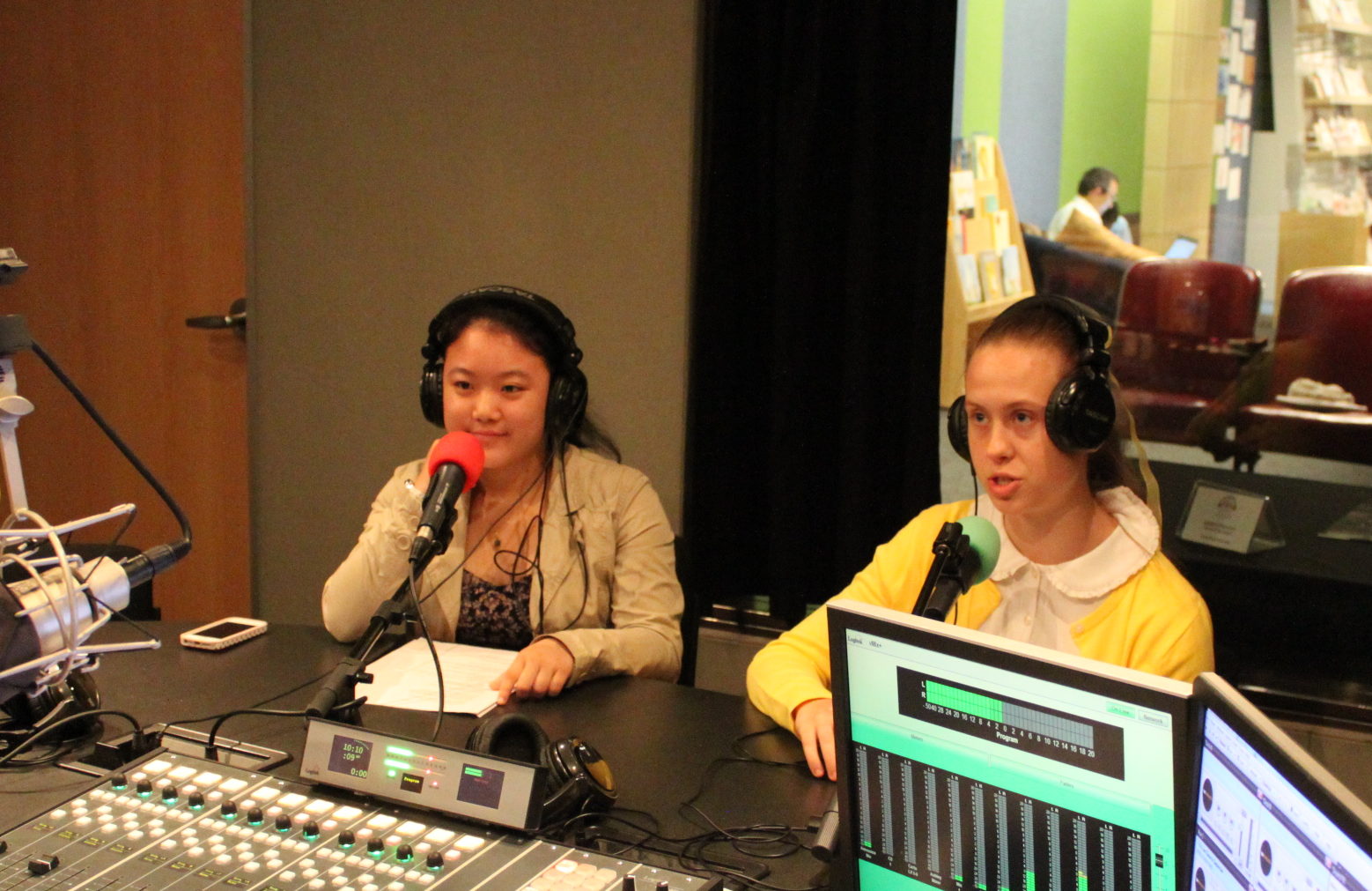 Two teens wearing headphones speaking into microphones in a radio studio