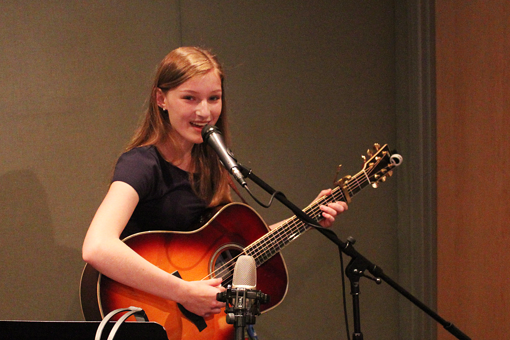 Teen playing acoustic guitar and singing into a microphone in a radio studio