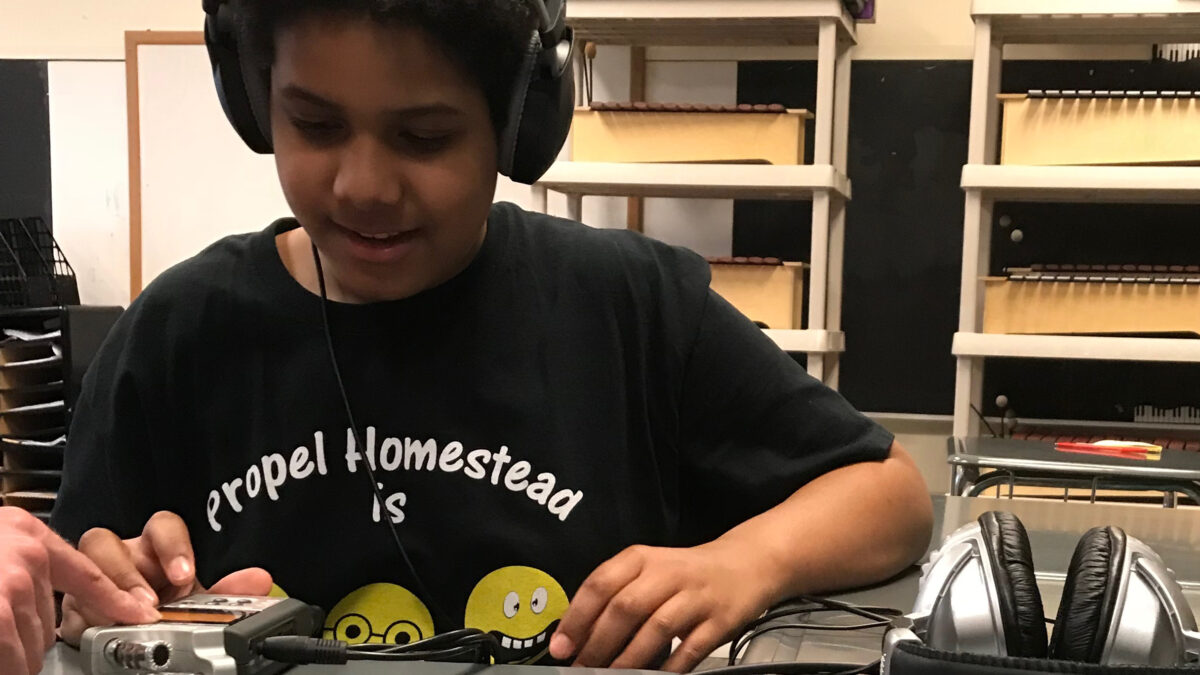 Youth wearing headphones listening to a portable recorder on a gray table