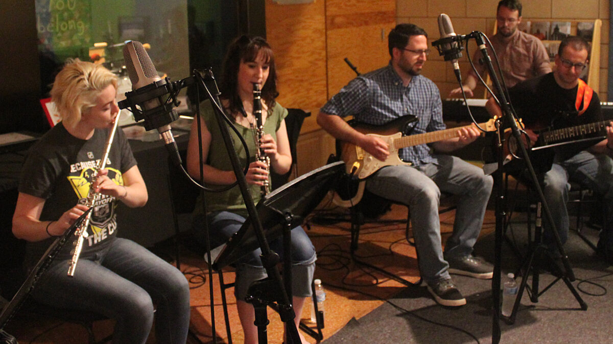 An adult playing flute, an adult playing clarinet, two adults playing electric guitar, and an adult playing a piano keyboard