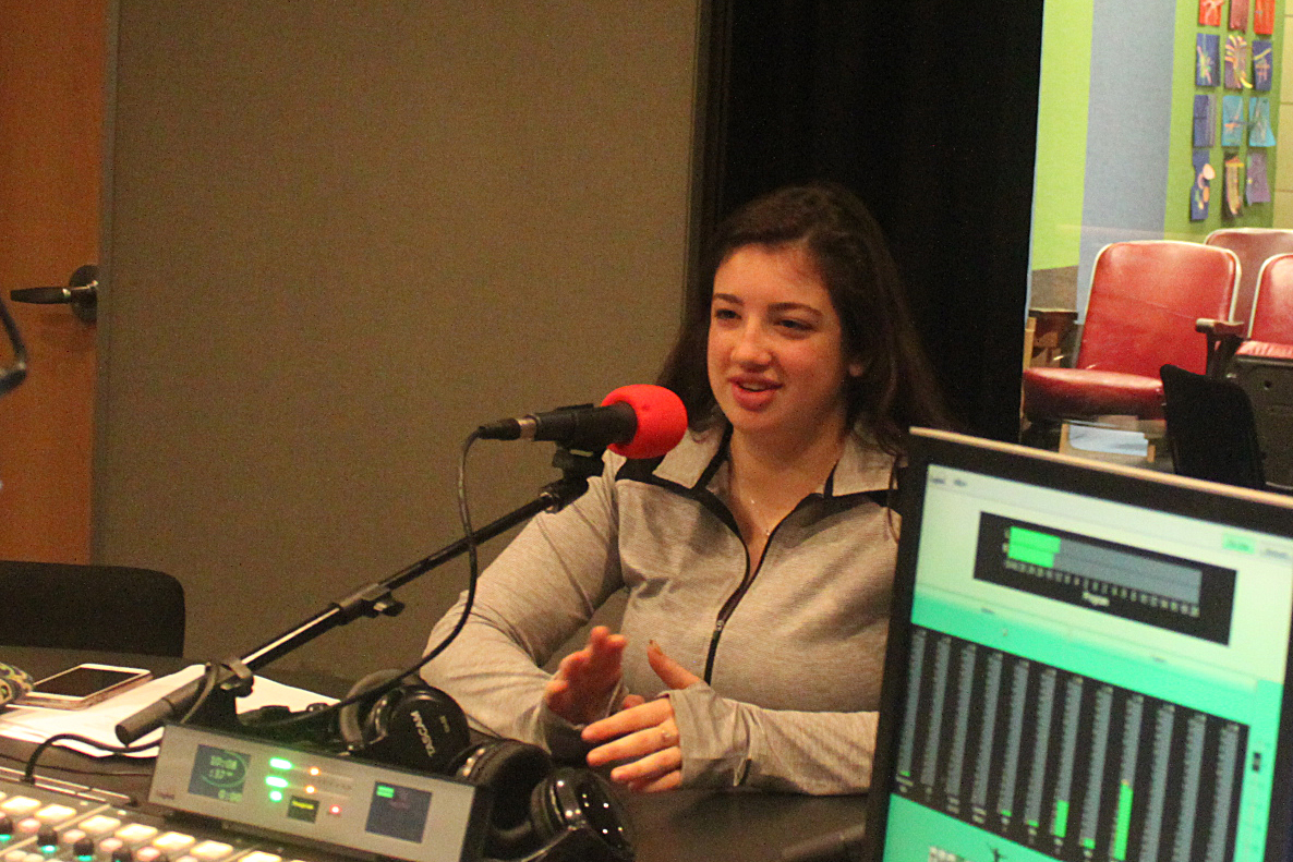 A teen talking into a microphone and gesturing with their hands being interviewed in a radio studio