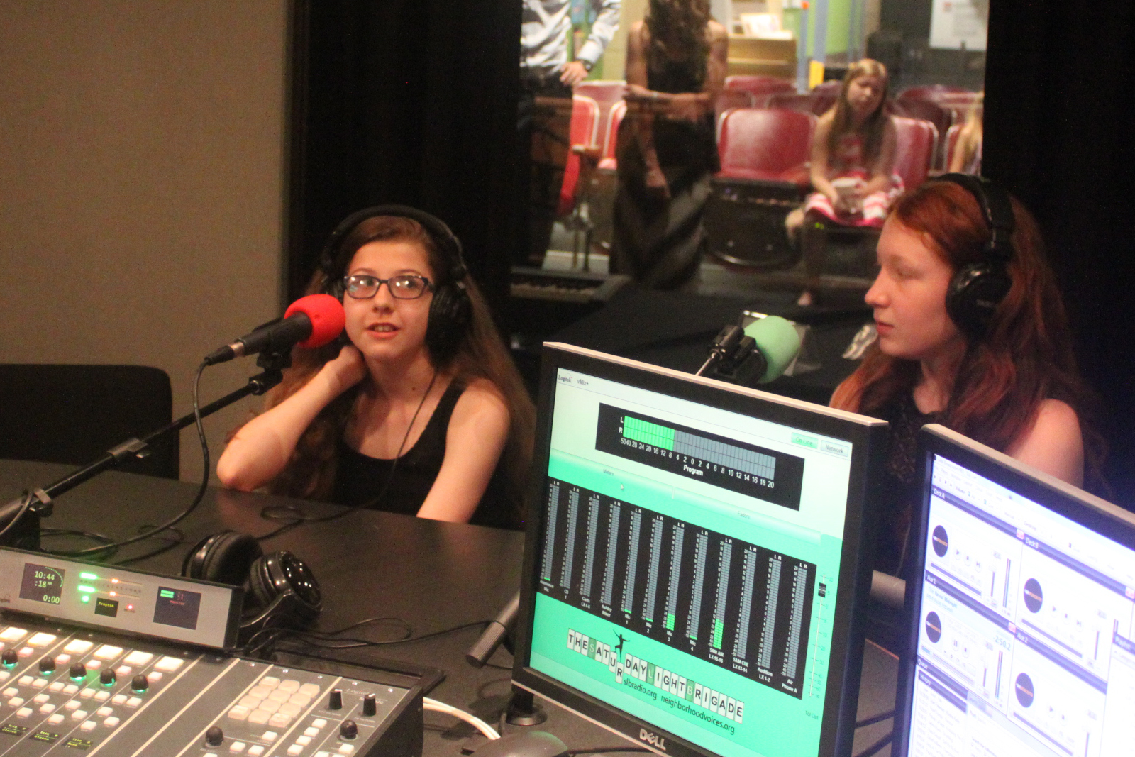 Two teens wearing headphones speaking into microphones being interviewed in a radio studio