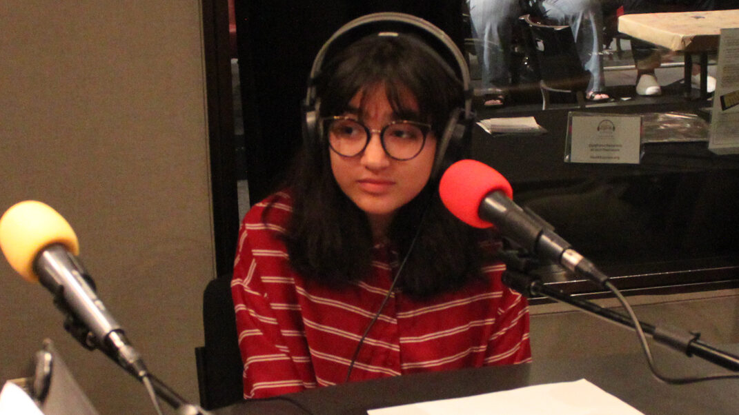 A youth wearing headphones sitting behind a microphone in a radio studio