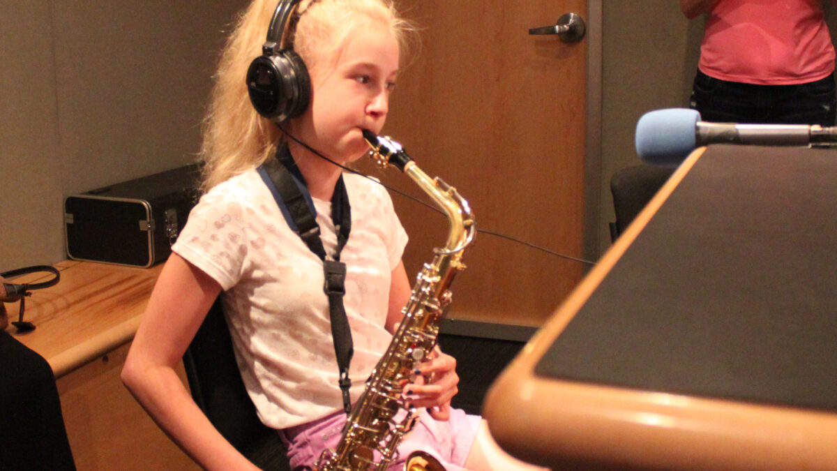 A youth wearing headphones playing an alto saxophone in a radio studio
