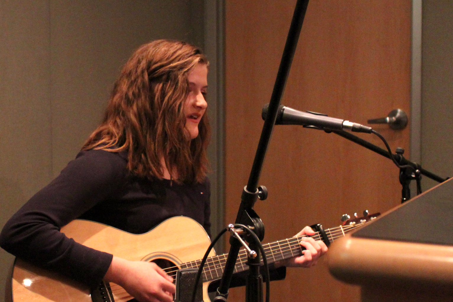 Teen playing acoustic guitar and singing into a microphone in a radio studio