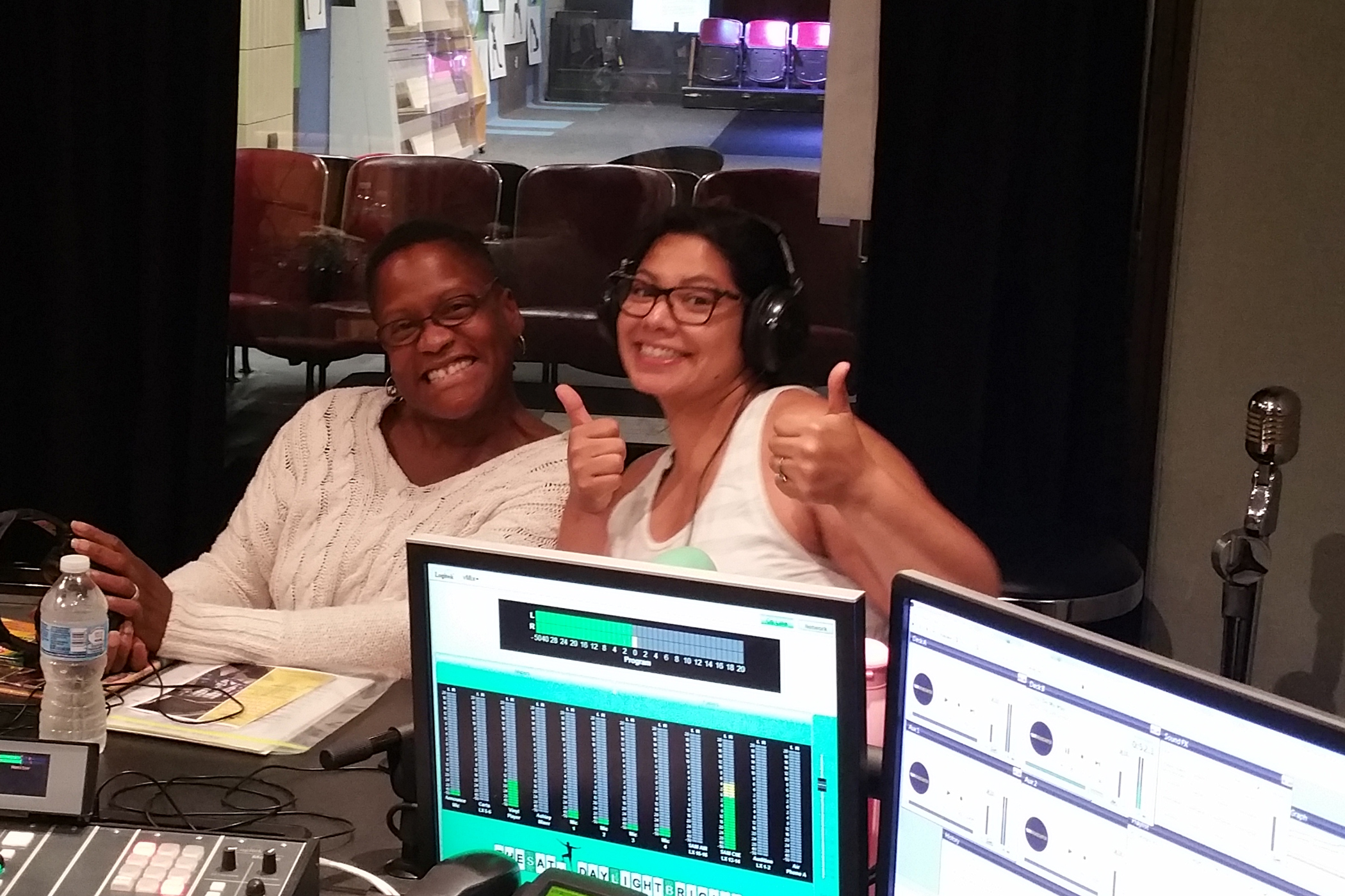 Two adults, one wearing headphones and giving two thumbs up, smiling in a radio studio